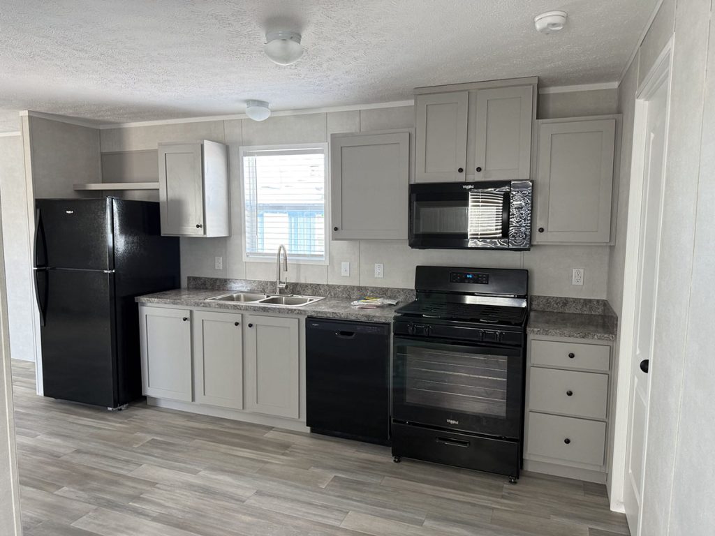 Modern kitchen with gray cabinets, black appliances including a fridge, stove, microwave, and dishwasher, marble-look countertops, and wood-look flooring. A window above the sink lets in natural light.