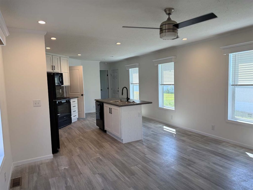 Modern kitchen with black appliances, white cabinets, island, and open floor plan. Light wood flooring, ceiling fan, and large windows letting in natural light.