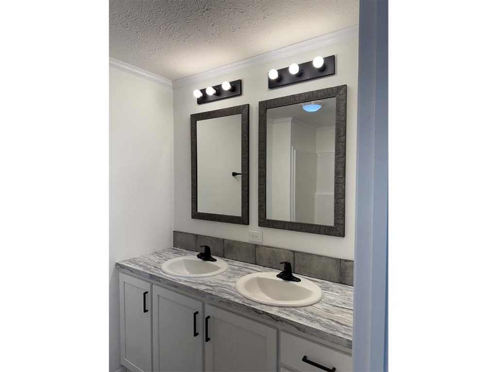 A bathroom features two sinks with marble countertops, two rectangular mirrors, and two black light fixtures, each with four bulbs, mounted above the mirrors.